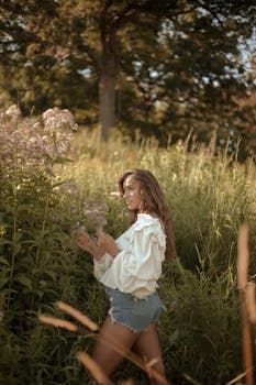A stylish woman in a meadow embraces nature during a sunny summer day.