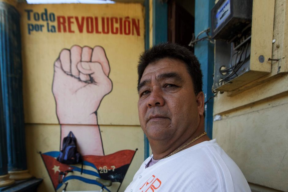 Man standing by a revolutionary mural with a raised fist and Cuban flag emblem.