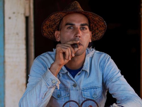 Free A man in a cowboy hat and denim jacket enjoys a cigar outdoors. Stock Photo