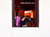 Three women chatting and enjoying leisure time by an open window, indoors with warm lighting.