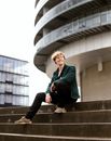Young Blonde Smiling Man Sitting on Stairs of Modernistic Building