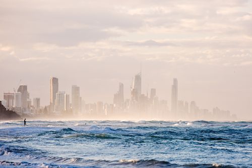Free Misty view of a city's skyline with waves and a lone figure on the beach at dawn. Stock Photo