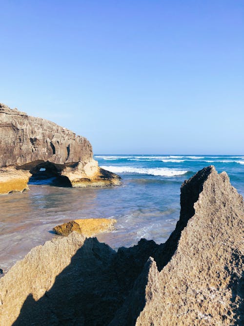 Brown Rocky Mountain Beside Blue Sea Under the Blue Sky