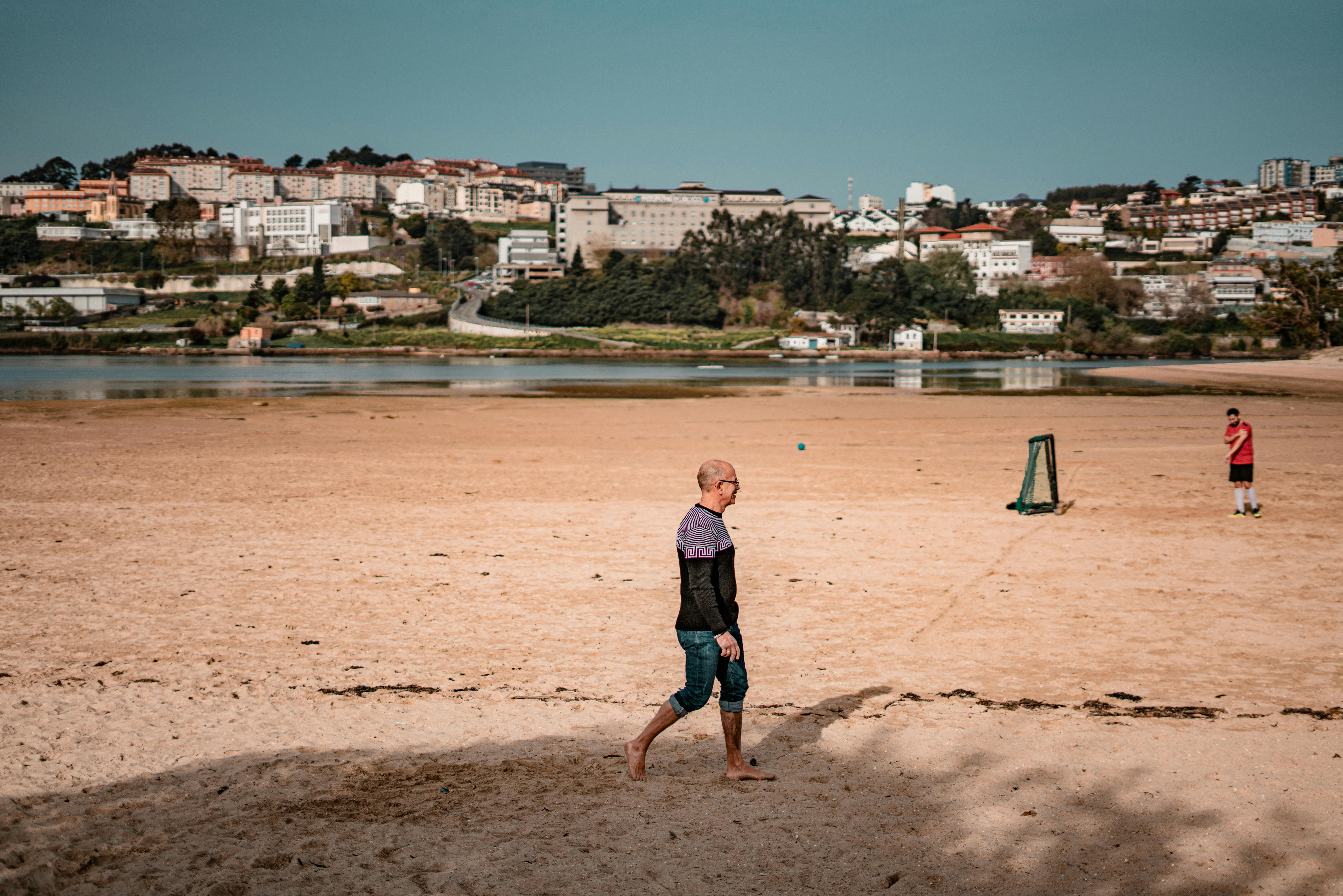 Man strolling on a sandy beach in Spain with urban backdrop. - Costa Brava