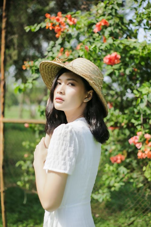 Free Elegant woman in a white dress and straw hat amidst vibrant flowers in Purwokerto, Indonesia. Stock Photo