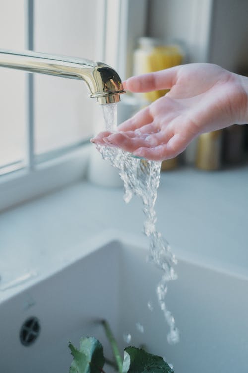 Free Woman Putting Her Hand Under Water Flowing From the Kitchen Tap Stock Photo