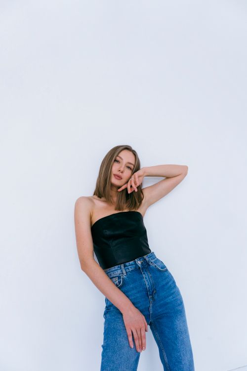 Free A young woman posing in a strapless black top and jeans, showcasing fashion style in a studio setting. Stock Photo