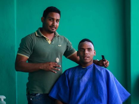 A barber standing next to his client wearing a cape in a vibrant barbershop setting.