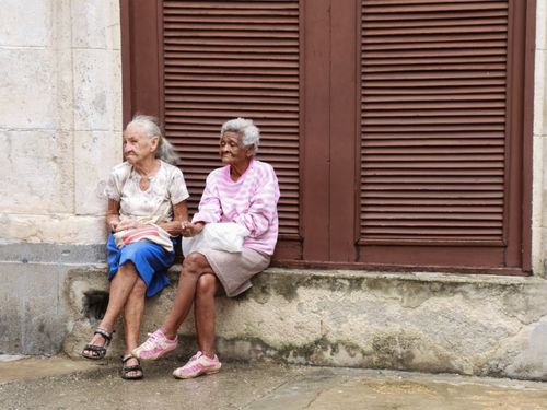 Free Two senior women sitting together with bags on a city sidewalk. Stock Photo