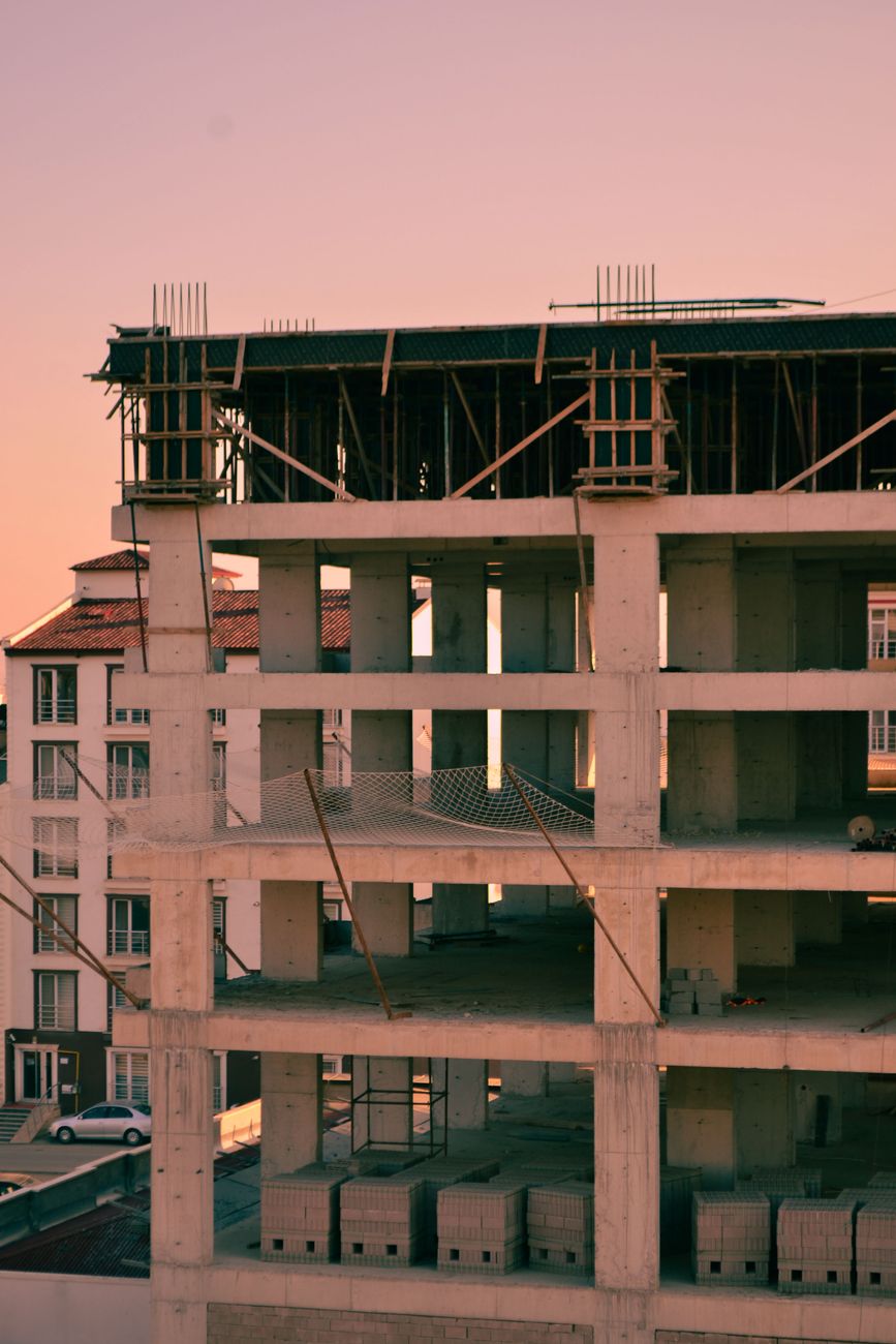High-rise building under construction with a sunset backdrop, highlighting urban development.