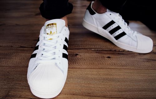 Free Close-up of trendy white sneakers with black stripes on a wooden floor, casual fashion look. Stock Photo