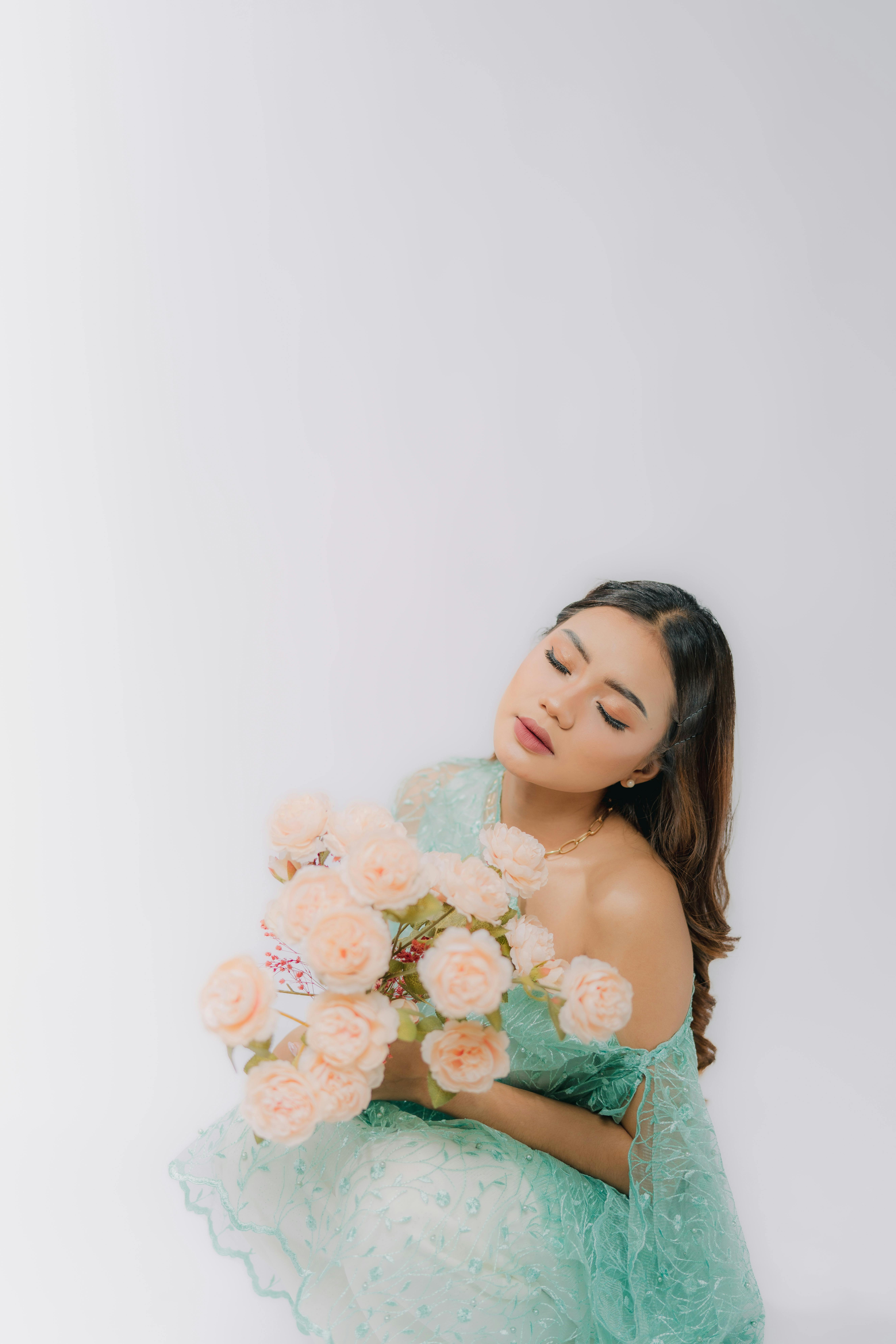 A young woman in an elegant dress holds a pastel bouquet, captured in a serene studio setting.