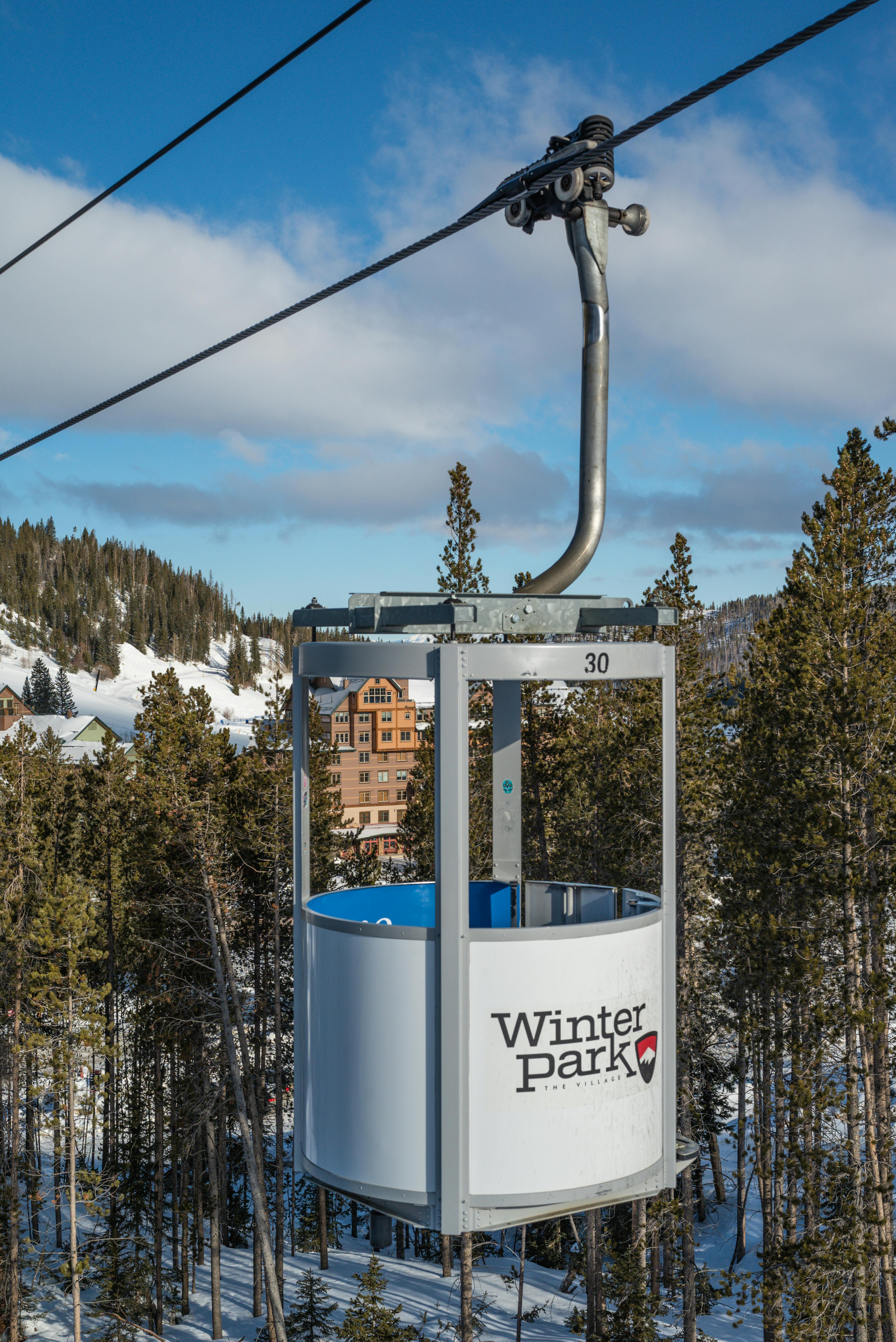 A picturesque ski lift at Winter Park resort surrounded by snowy mountains and trees.