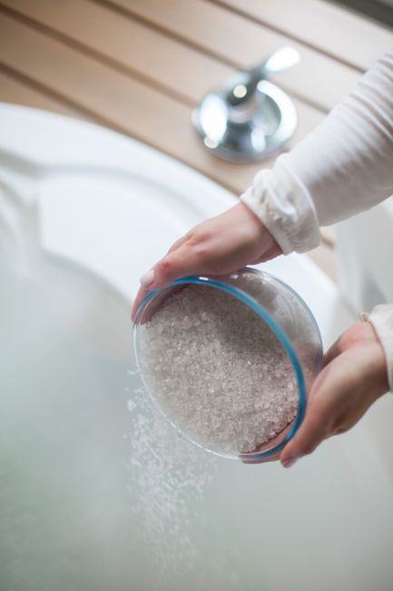 Fotomural Una mujer vierte sales de baño en un jacuzzi, creando una atmósfera de spa lujosa y relajante.