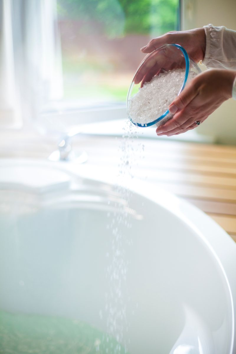 Hands pouring sea salt into a bathtub