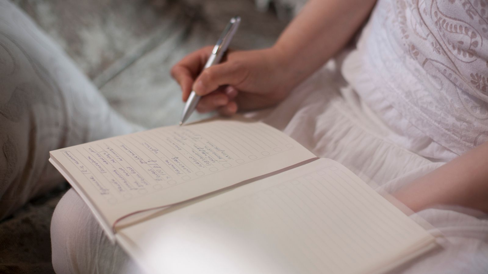 A hand holding a pen above an open notebook on a lap