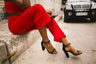 在城市环境中，一位穿着红色裤子和黑色高跟鞋的时尚女人坐着