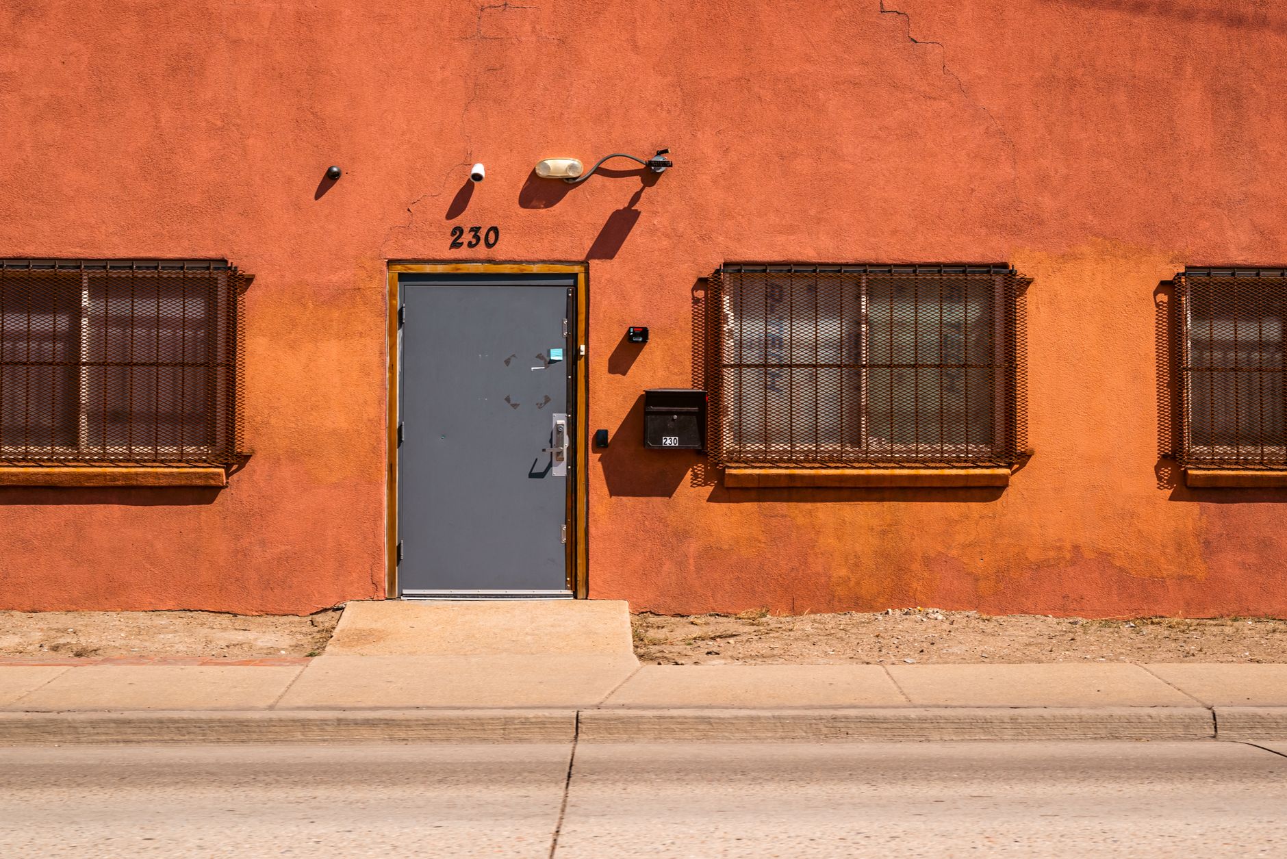 An orange facade with a sturdy metal door and barred windows under bright daylight.