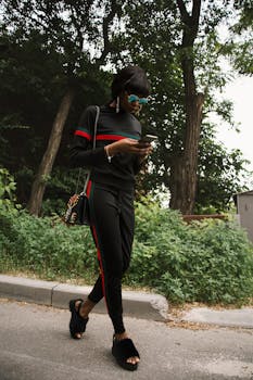 一位穿着时尚的年轻女子在户外行走，查看手机，周围绿意盎然