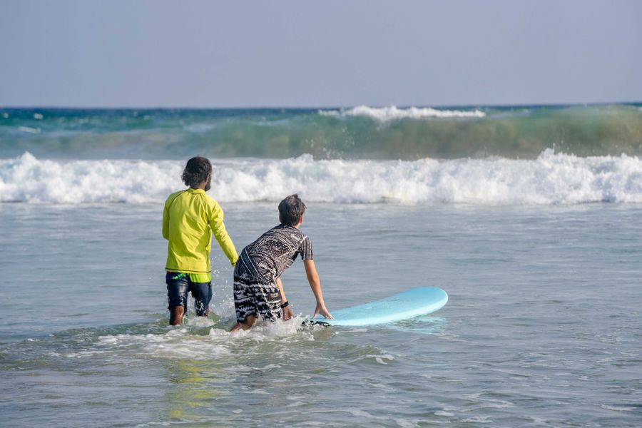 Two surfers heading into the ocean with a board
