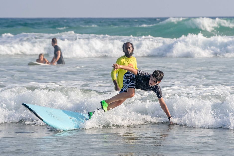 A teenager learning to surf with an instructor in a sunny beach setting.