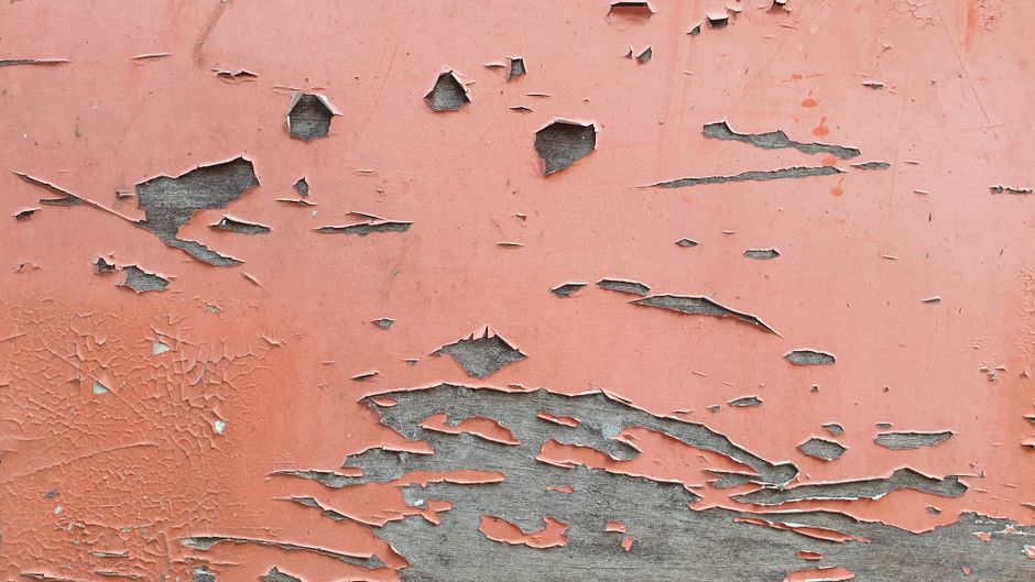 person scraping peeling paint from wall with putty knife