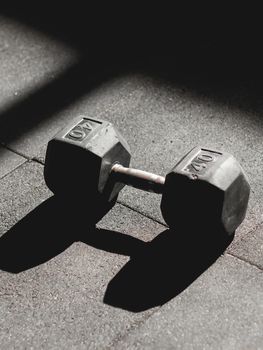 A single dumbbell casting a shadow on a textured gym floor, perfect for fitness and workout themes.