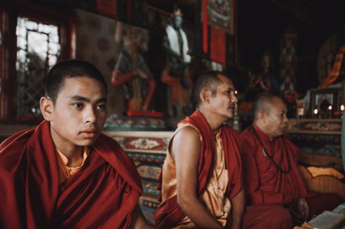 Free Three Buddhist monks in red robes sit inside a richly decorated temple during a sacred ceremony. Stock Photo