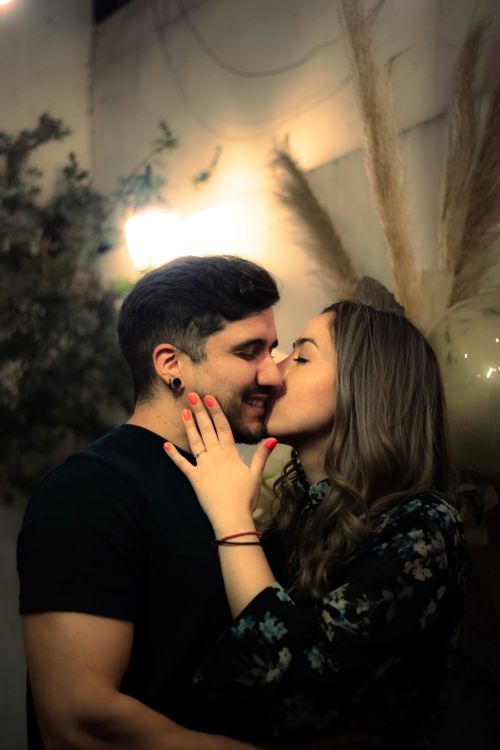 Free A young couple shares a tender kiss in a dimly lit indoor setting, exuding love and happiness. Stock Photo