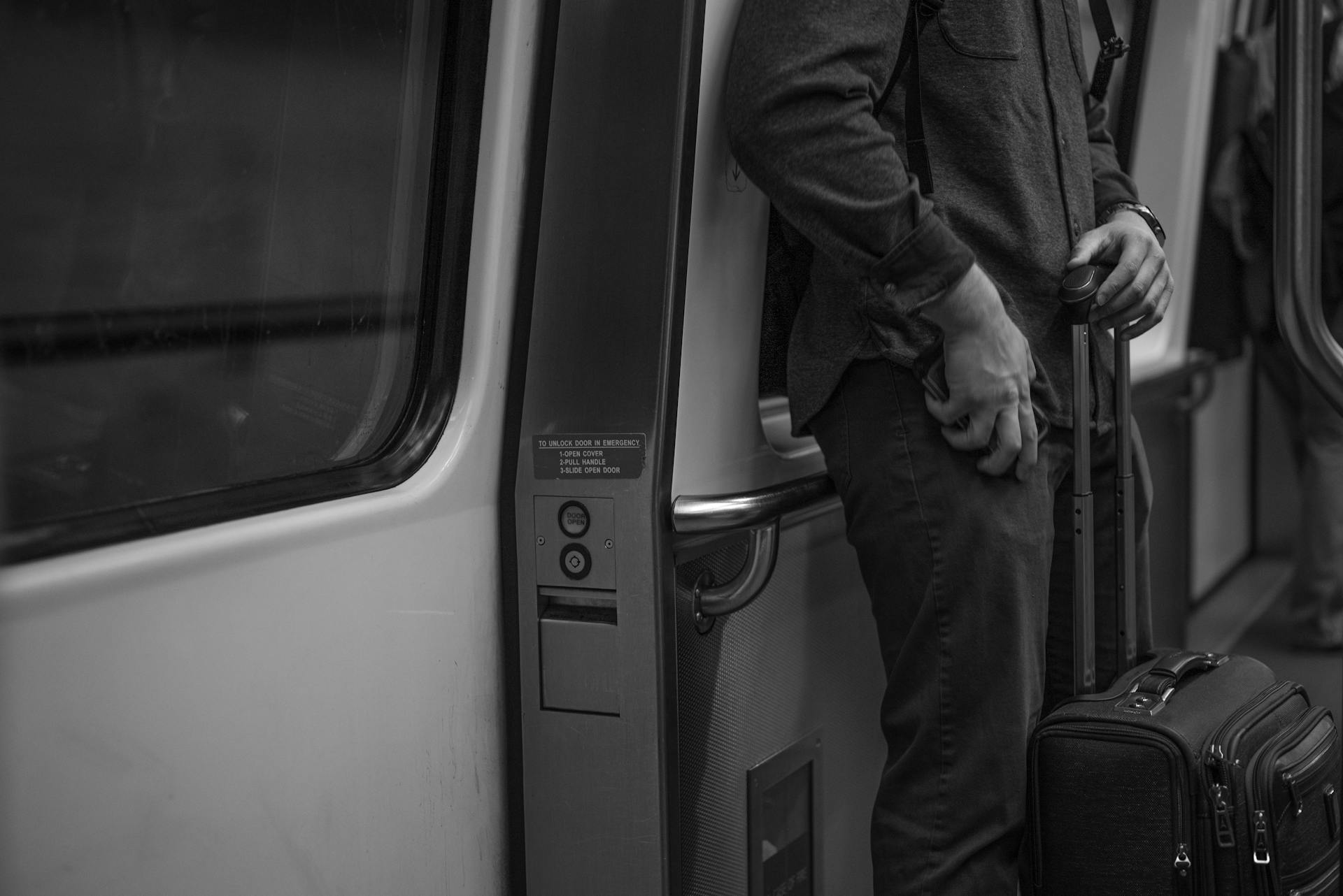 Man standing with luggage in train, reflecting travel and journey in monochrome.