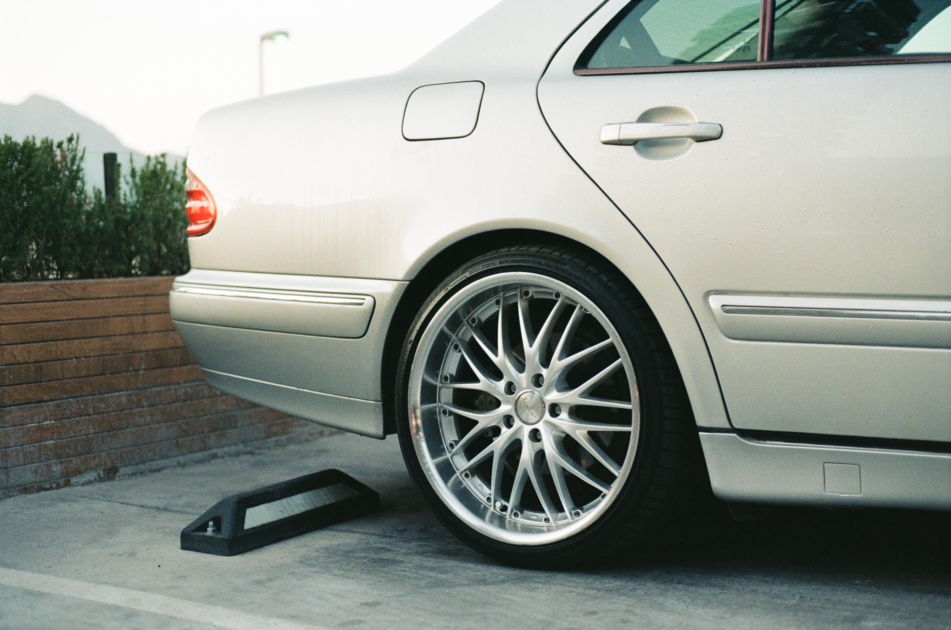 Detailed view of a luxury car's rim and tire on a silver vehicle in an outdoor parking lot.