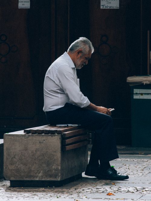 Free Side view of an elderly man sitting on a bench in São Paulo, Brazil, deep in thought. Stock Photo
