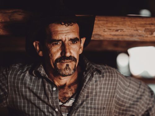 Free Portrait of a rugged man wearing a cowboy hat and checkered shirt, looking pensive. Stock Photo
