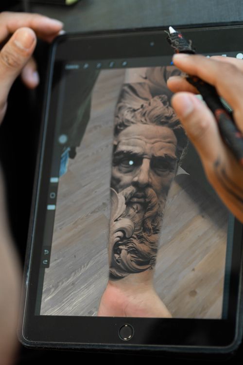 Free Artist designing intricate tattoo on tablet using digital tools in studio setting. Stock Photo
