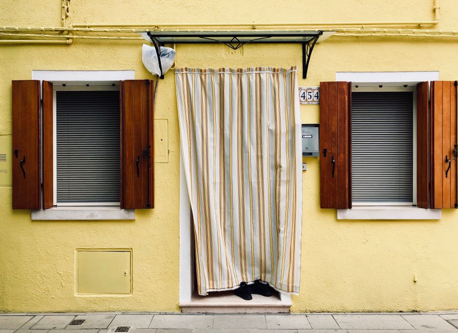 Charming yellow facade with wooden shutters and striped curtain in Venice, Italy.