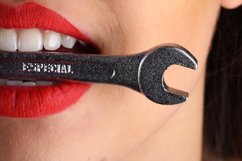 Close View of Woman With Red Lips Biting Gray Special Wrench