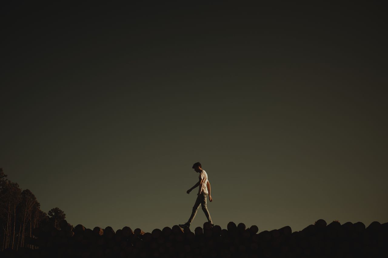 a person silhouetted in twilight walking on logs creating an introspec