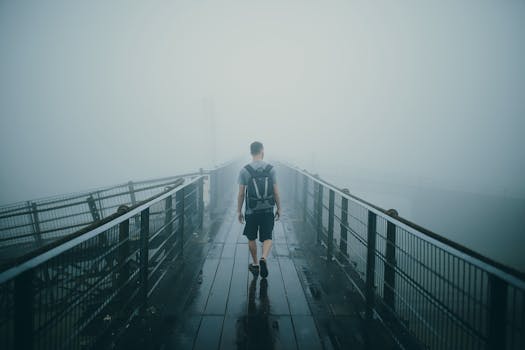 A lone man with a backpack walks across a misty bridge, creating a mysterious atmosphere.