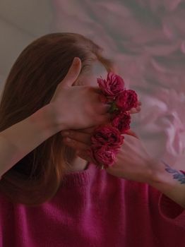 Artistic portrait of a woman covering her face with pink flowers in a pink sweater.