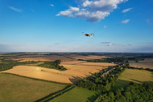 Drone captures vibrant rural landscape with fields and trees under clear blue sky.