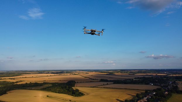 A drone captures the expansive agricultural fields of the English countryside under a clear blue sky.