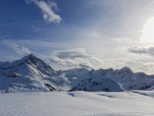 A Snow Covered Ground with Mountains Under the Blue Sky and White Clouds