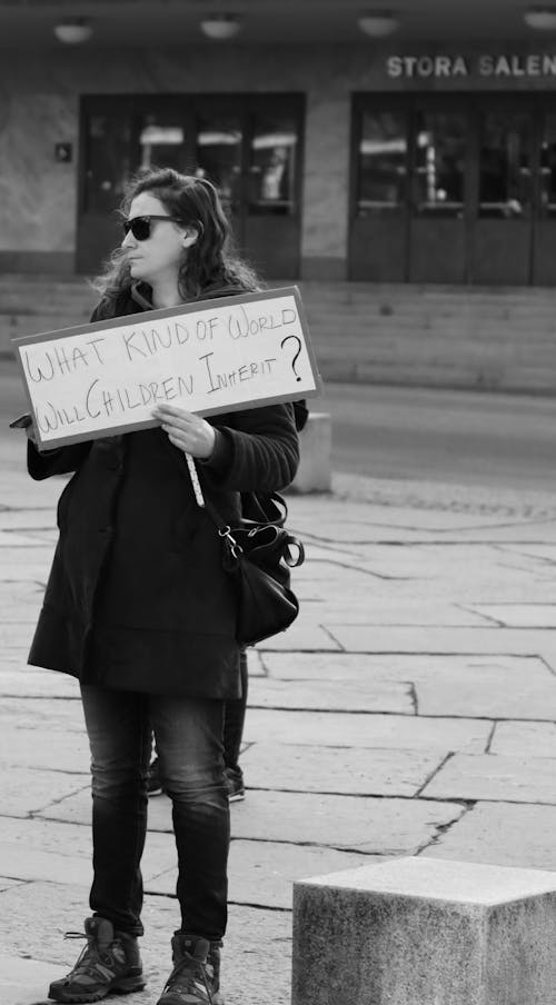 A Grayscale Photo of Woman Holding a Placard Standing on the Street