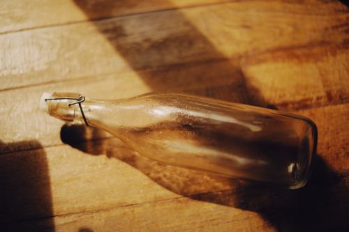 Free A glass bottle lies on a sunlit wooden floor, casting shadows, creating a warm ambience. Stock Photo