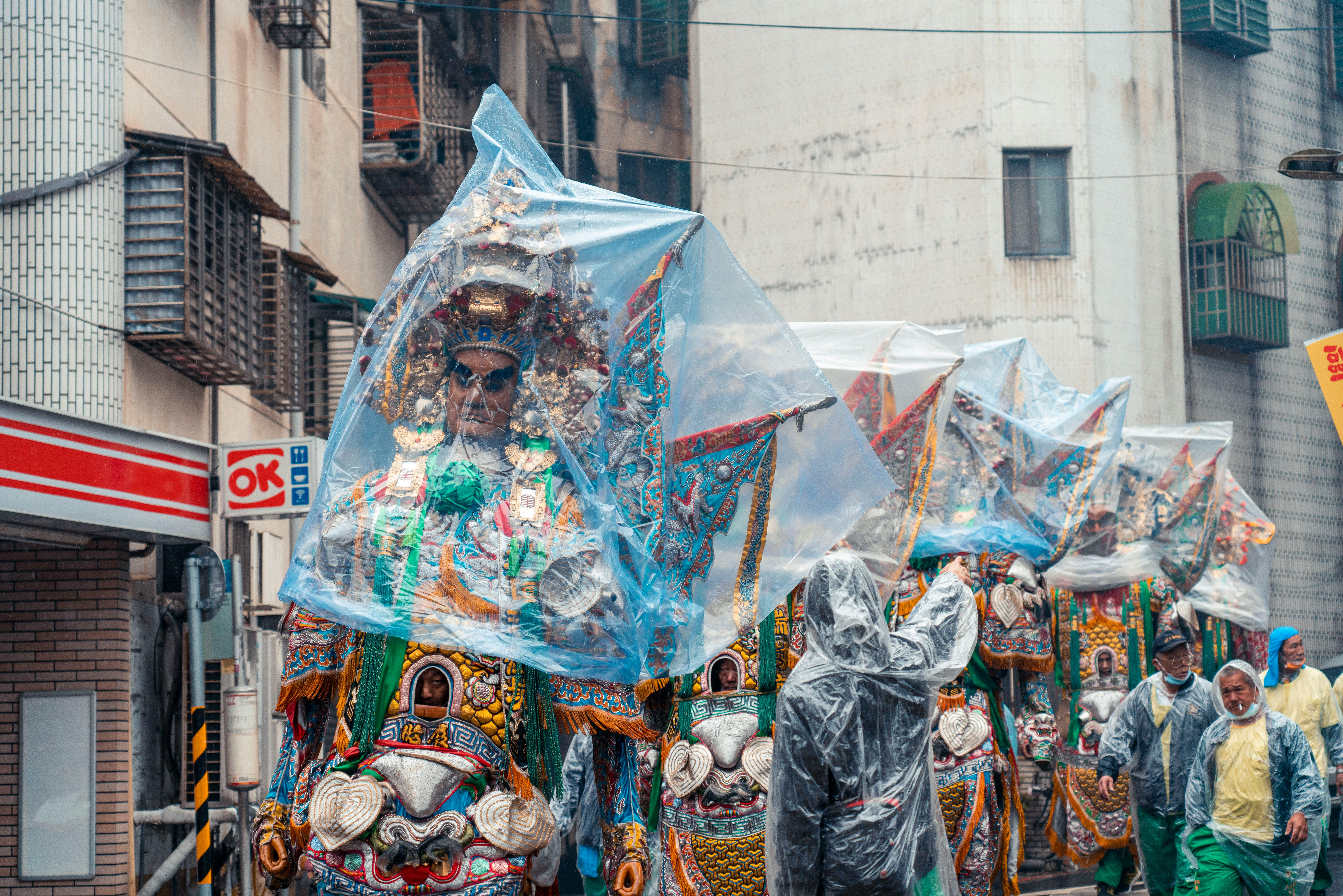 Vibrant street parade featuring traditional costumes covered due to rain.