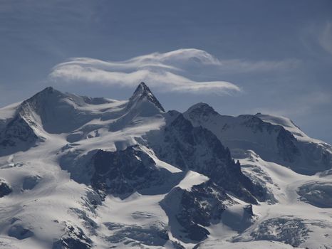 Majestic snowy mountain peaks with dramatic clouds against a blue sky, offering a breathtaking scenic view.