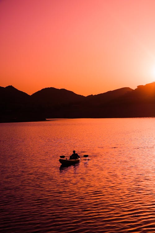 Silhouette of a Person Riding a Boat and Mountains during Sunset