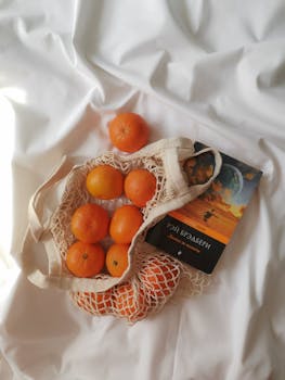 Net bag filled with oranges next to a book, promoting eco-friendly lifestyle and healthy eating.
