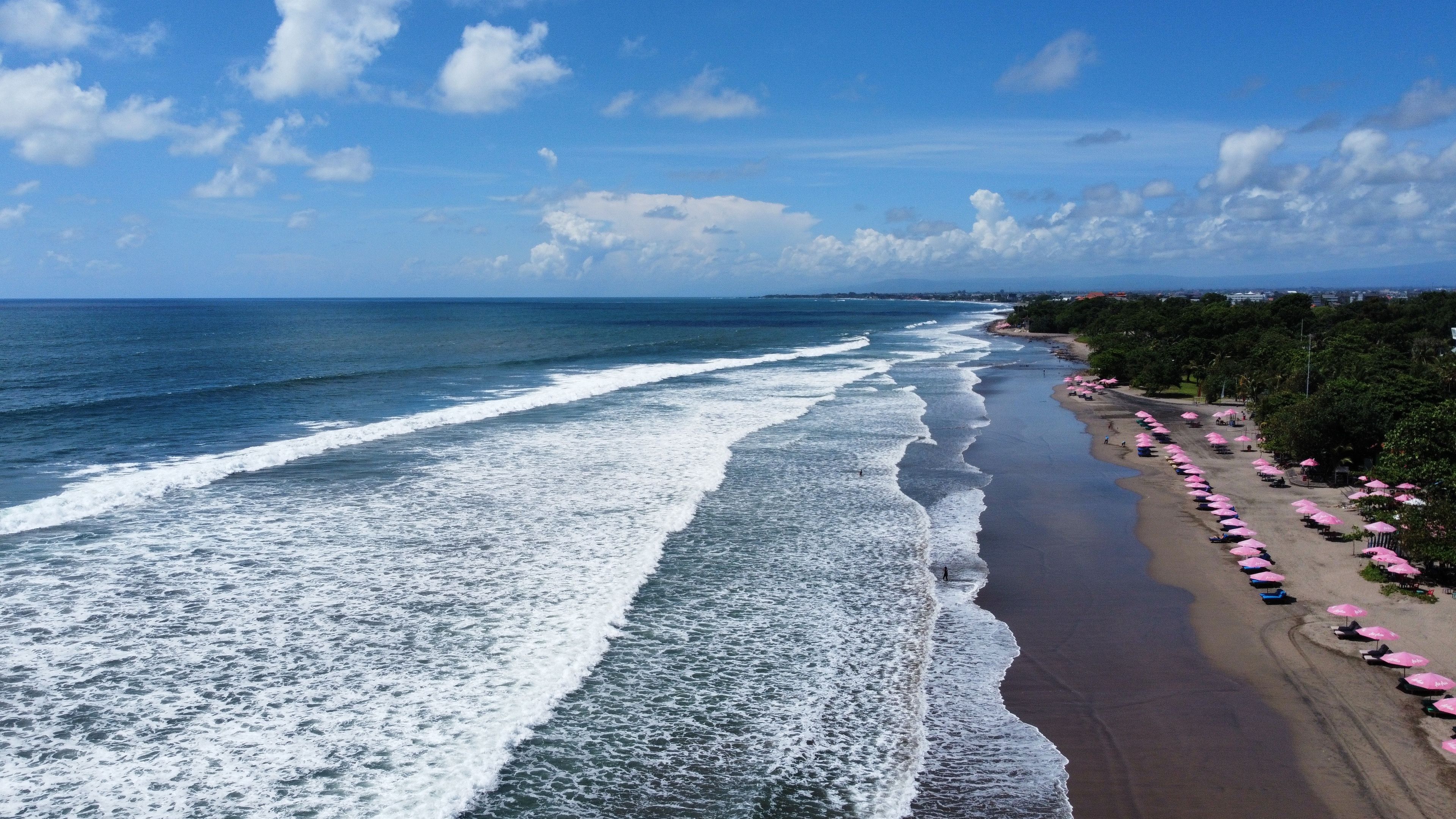 Breathtaking aerial view of Bali's beach with vibrant pink umbrellas and waves crashing on the shore.