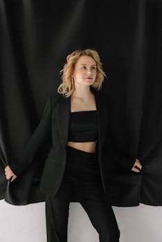 Elegant blonde woman wearing a black suit poses confidently against a dark backdrop in a studio setting.